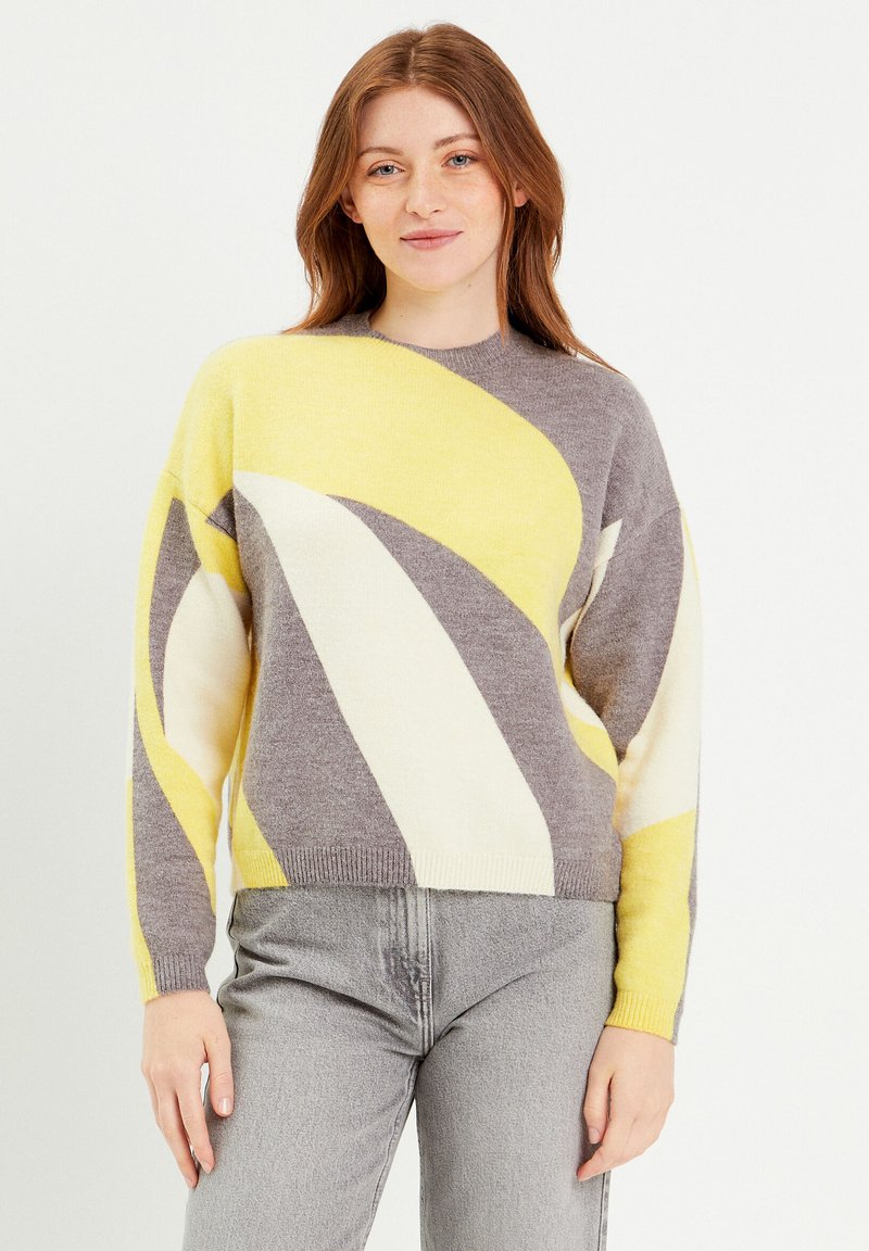 Pull en tricot gris, crème et jaune avec un motif géométrique. Il possède un col rond et de longues manches. Tissu doux et texturé.