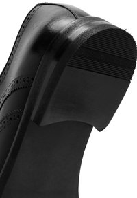 Zapato de vestir de cuero negro que muestra la suela detallada, el tacón y perforaciones al estilo brogue en la parte superior lisa.