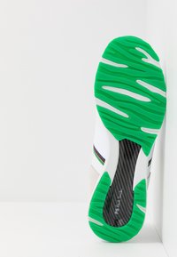 Grüne und weiße Sneaker-Sohle mit einer strukturierten GummOberfläche. Verfügt über einen Bereich aus Kohlefaser, einen farbigen Streifen und wellenförmige Designelemente.