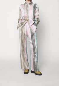 Dvousložkový outfit zahrnující světlou růžovou a zelenou pruhovanou košili a odpovídající kalhoty. Hladká látka s detailem knoflíku a širokým střihem nohavic.