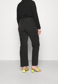 Jeans neri in denim a vita alta con taglio a gamba dritta, dotati di due tasche posteriori. Abbinati a sandali con tacco a blocco giallo.