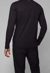 Czarna, długorękawowa koszula wykonana z bawełny, z okrągłym dekoltem i małym logo z tyłu. Gładka faktura i dopasowany krój.