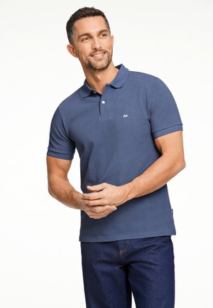 Dunkelblaues Polohemd aus strukturiertem Baumwollstoff, mit einer Knopfleiste mit drei Knöpfen und einem kleinen Logo auf der linken Brust. Kombiniert mit dunklen Jeans.