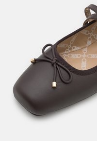 Chaussure plate marron foncé avec un bout carré, nœud décoratif avec embouts dorés et doublure intérieure beige à motifs.