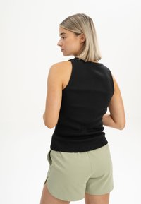 Schwarzes, geripptes Tanktop mit einer taillierten Passform und rundem Ausschnitt, kombiniert mit hellgrünen Shorts mit Seitentaschen.