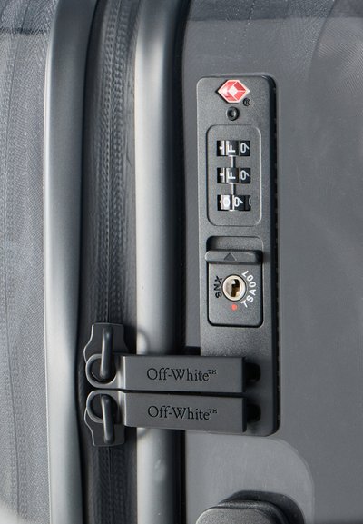 Λουκέτο συνδυασμού με κλειδαριά TSA σε μαύρη βαλίτσα, με δύο τσόκους φερμουάρ επώνυμους Off-White που ασφαλίζονται μέσω του λουκέτου.