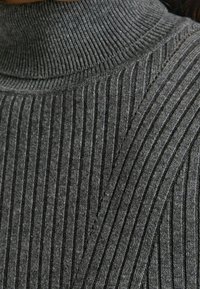 Grå rippad tröja med hög krage. Har strukturerade vertikala ränder och en tajt passform som framhäver det mjuka stickade materialet.