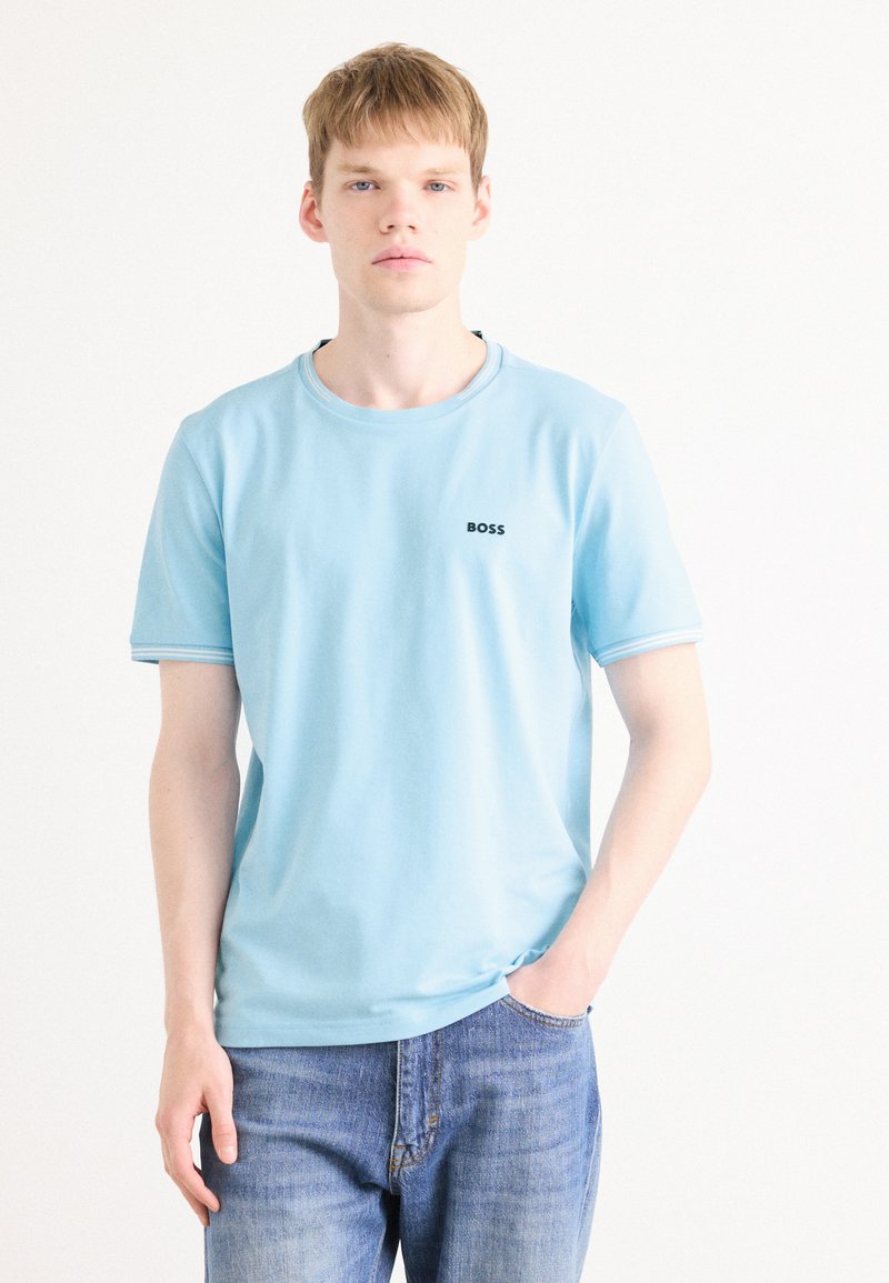 T-shirt en coton bleu clair avec un col rond, des manches courtes et un petit logo noir "BOSS" sur la poitrine gauche. Coupe décontractée.