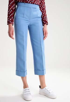 Pantalons ajustés bleu clair à taille haute, avec deux pinces à l'avant et des poignets retroussés, associés à des baskets blanches.