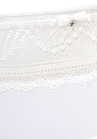 Witte lingerie met complexe kantdetails bij de tailleband. Heeft een zachte textuur, delicate accenten en een kleine strikversiering.