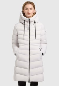 Long white puffer coat with a high, padded collar, black zipper, and drawstrings. Features horizontal quilted sections and side pockets.