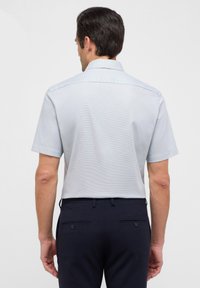 Camicia a maniche corte di colore azzurro chiaro con motivo a quadri, dotata di colletto classico e trama liscia, abbinata a pantaloni scuri.