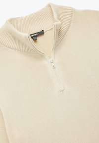 Beige Sweatshirt mit Reißverschluss, hergestellt aus gestricktem Stoff. Verfügt über einen hohen Kragen sowie eine gerippte Textur entlang des Kragens und der Bündchen. Klassische Passform und einfaches Design.