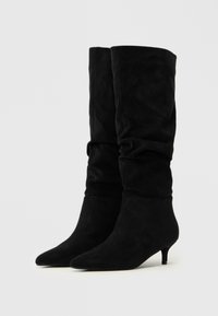 Bottes noires, montantes jusqu'aux genoux, en suède doux. Présentent un design décontracté, un bout pointu et un petit talon. Pas d'ornements ni de motifs visibles.