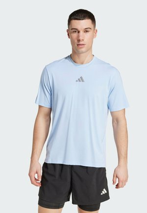 Maglietta sportiva azzurra chiara a maniche corte, realizzata in tessuto morbido, con un logo grigio sul petto. Indossata con pantaloni corti neri.