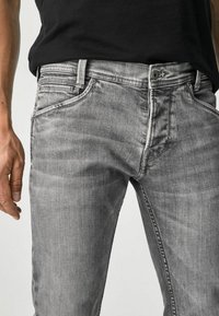 Vaqueros de denim gris con corte ajustado, que presentan sutiles detalles desgastados, cinco bolsillos y herrajes de botón en tono plateado.