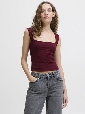 Débardeur bourgogne ajusté avec un col carré, associé à un jean gris taille haute légèrement déchiré. Matière douce, design minimaliste.