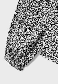 Tessuto floreale in bianco e nero con dettagli a maniche svasate, caratterizzato da piccoli fiori ripetuti su una superficie testurizzata.