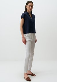 Haut en lin bleu marine avec un col en V et des manches courtes, associé à un pantalon en lin blanc et des sandales à lanières marron. Design simple et décontracté.