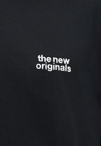 Mustast kangast, mille keskel nähtaval alal on väikesed valged tikitud tähed "the new originals".