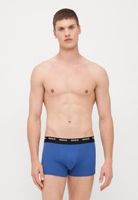 Blå bomullsboxershorts med svart elastisk midjeband som har "HUGO"-logotypen i vitt. Fitted design, slät textur.