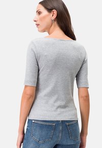 Graues kurzärmeliges Oberteil aus weichem Material mit rundem Ausschnitt, kombiniert mit blauen Jeans aus Denim im klassischen Taschenstil.