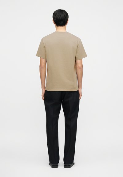 Ανοιχτό καφέ βαμβακερό μπλουζάκι με κοντά μανίκια και στρογγυλή λαιμόκοψη, σε συνδυασμό με μαύρο, ραμμένο παντελόνι, βλέπουμε από πίσω.