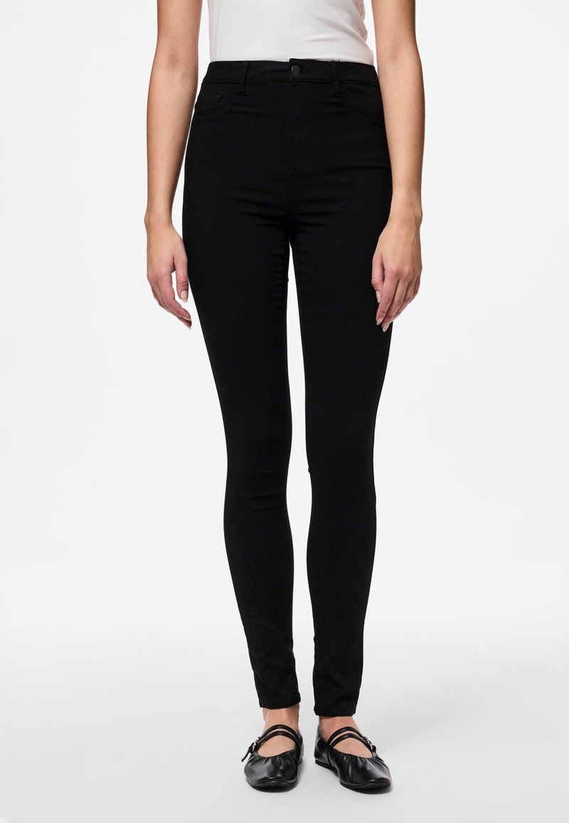 Jean noir slim-fit à taille haute, avec une texture lisse et un design classique à cinq poches. Accompagné de chaussures plates noires.