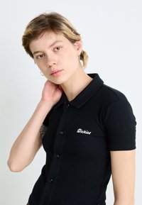 Polo preto com riscas, de mangas curtas, design ajustado, fecho com botões e logótipo "Dickies" bordado na área do peito esquerdo.