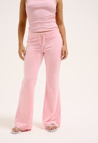 Roze uitlopende sweatpants en een bijpassende tanktop, beide gemaakt van zachte stof. De broek heeft een trekkoord en decoratieve rhinestone accenten.
