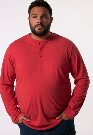 Červená dlouhá košile henley s dlouhým rukávem vyrobená z měkké tkaniny, se třemi knoflíky u výstřihu a jemným logem na hrudi. Hladká struktura.