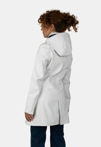 Cappotto impermeabile bianco con cappuccio, caratterizzato da un design elegante, fessure laterali e una texture liscia. Indossato sopra jeans scuri.