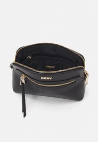 Black leather handbag with gold hardware, zip closure, and interior pockets. Features DKNY logo. Textured outer material. Compact design.