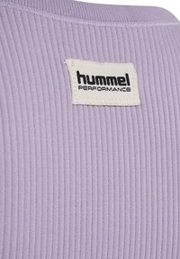 Tissu côtelé lilas avec une étiquette rectangulaire blanche cousue, affichant "hummel PERFORMANCE" en texte noir.