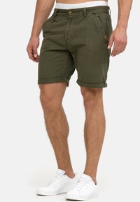 Olivengrønne shorts lavet af bomuld, med opklemmede kanter, forlommer og knaplukning. Bæres med hvide sneakers for kontrast.