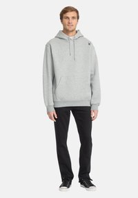 Felpa grigia con cappuccio, tasca frontale, collo con cordino, polsini e orlo a costine. Abbinata a pantaloni neri e sneakers nere.