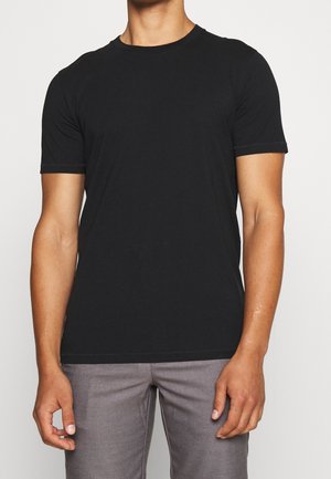 Camiseta de algodón negra con escote redondo y mangas cortas, que presenta una textura suave y un diseño simple, combinada con pantalones grises.