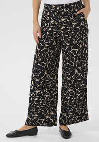 Pantalons larges noirs avec un motif abstrait beige. Le tissu a une finition texturée. Comprend des poches latérales et une coupe décontractée.
