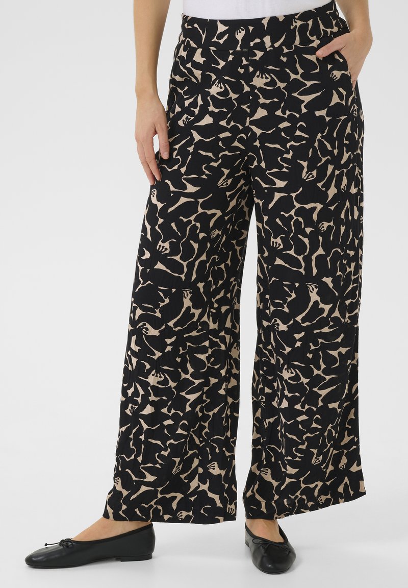 Pantalons larges noirs avec un motif abstrait beige. Le tissu a une finition texturée. Comprend des poches latérales et une coupe décontractée.