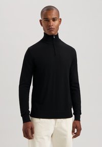 Maglione nero con zip, colletto alto, maniche lunghe e polsini a coste. Realizzato in tessuto morbido, presenta una silhouette aderente e linee pulite.