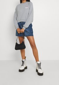 Sweatshirt gris coupé, jupe en denim, sac à main noir et bottes blanches à lacets avec semelles épaisses. Détails du logo sur le sweatshirt.