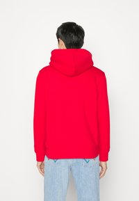 Red hooded sweatshirt with a soft texture, ribbed cuffs, and waistband. The back features a simple design, paired with light blue jeans.