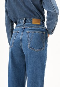 Jeans i denim i medelblå färg med hög midja, rak benprofil, fem fickor och en brun läderetikett på baksidan.