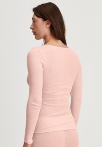 Long-sleeve, ribbed top in soft pink. Features a rounded neckline and fitted silhouette, made from lightweight, textured material.