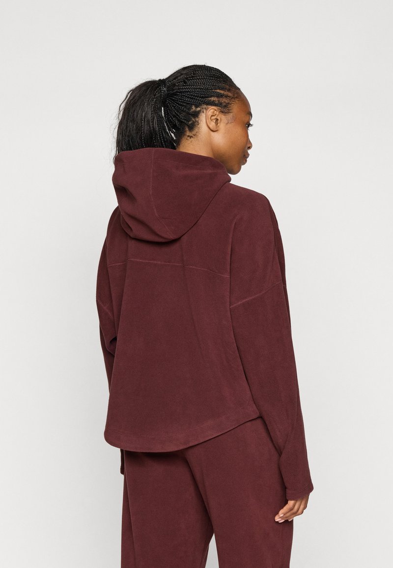 Felpa con cappuccio bordeaux in morbido tessuto, vestibilità rilassata e spalle scese. Presenta un orlo curvo e dettagli di cucitura minimali.