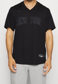 Musta Nike v-paita, jossa on kohotettu "NEW YORK" -painatus. Lyhyt hiha, kevyttä kangasta, pieni logo vasemmassa olkapäässä.