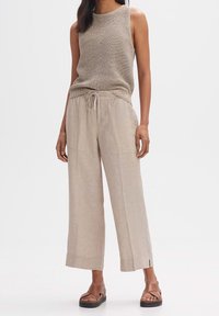 Un haut sans manches en tricot beige associé à un pantalon en lin large beige clair avec poches et cordon de serrage. Des sandales marron complètent la tenue.