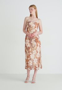 Strapless bloemenjurk met een getailleerde bovenkant, vloeiende rok en een perzikbruin kleurenpalet met witte bloemen. Zachte, doorzichtige stof.