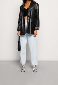 Černý blazer z umělé kůže přes černý crop top, v kombinaci s světle modrými širokými džínami a kotníkovými botami se zebřím potiskem, doplněný černou taškou.