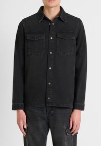 Zwarte denim shirtjack, met een kraag, twee voorkruiszakken met decoratieve stiksels en metalen drukknoopsluitingen.